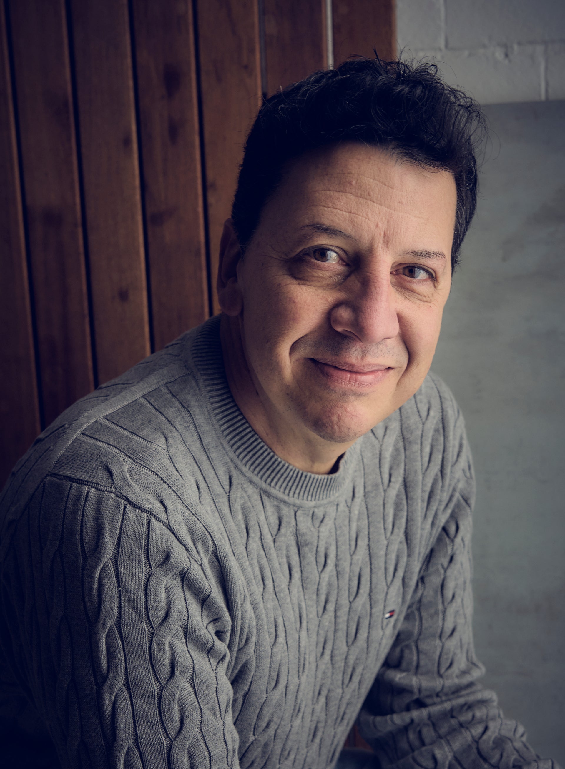 Luca Chiaravalle of Gotham Studios Collective wearing a gray cable knit sweater against a wooden panel background