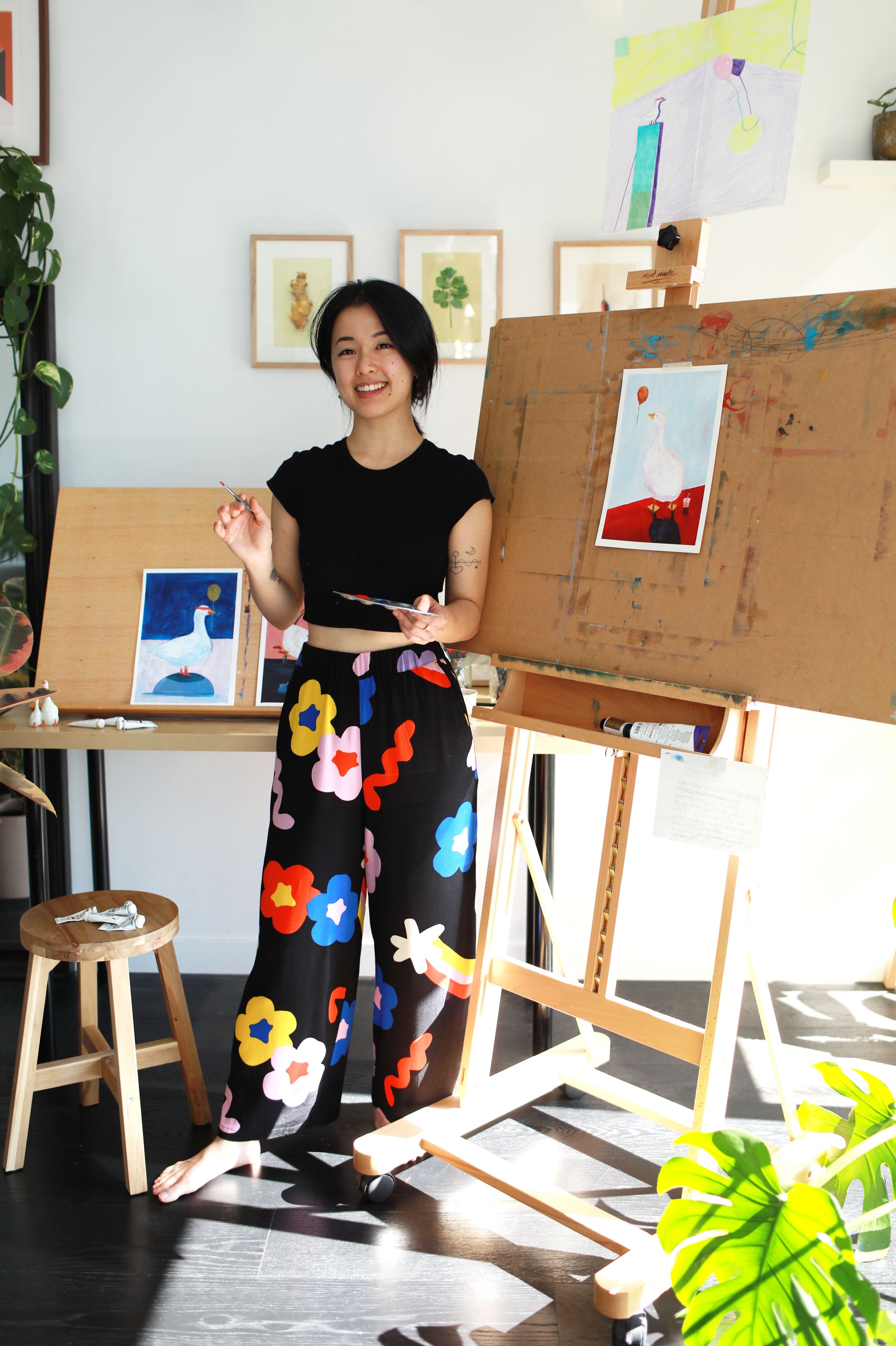 Sheng Yi Lee of Gotham Studios Collective in a colorful dress standing next to an easel with art in a studio setting